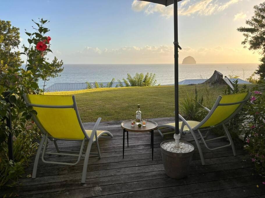 2 Stühle, ein Tisch und ein Regenschirm auf einer Terrasse in der Unterkunft Studio vue mer avec piscine in Le Diamant