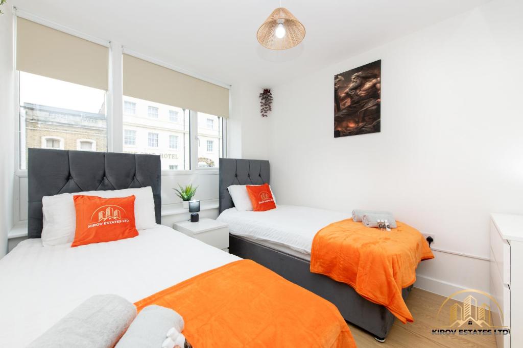 2 bedden in een kleine kamer met oranje kussens bij Hephaestus Apartment - The Craftsman of Town in Southampton