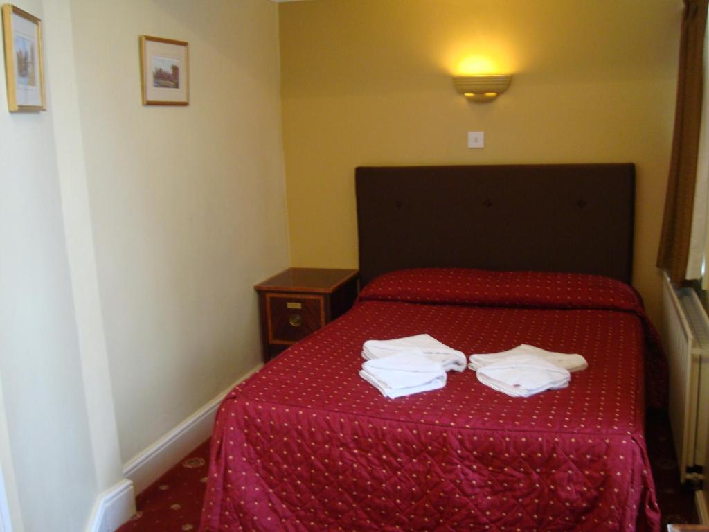 um quarto com uma cama vermelha e 2 toalhas brancas em Rose Court Hotel em Londres