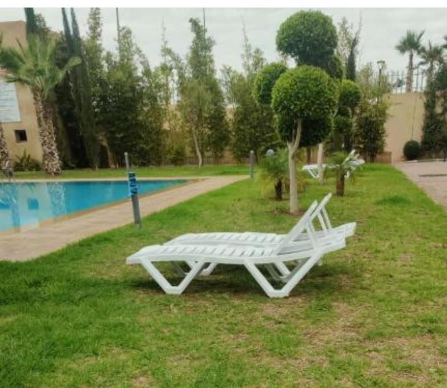 a white bench sitting in the grass next to a pool at Appartement de rêve à Marrakech in Marrakech