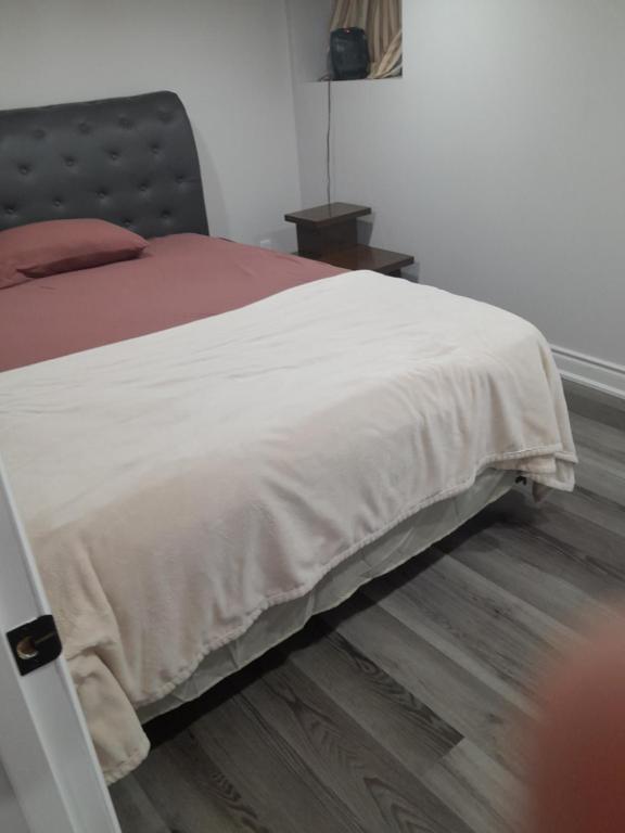 a bed with a white blanket on top of a wooden floor at Downtown closer place for rest in Hamilton