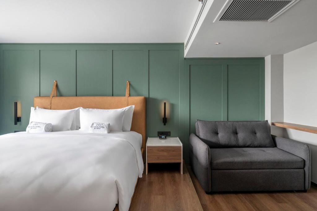 A bedroom with a large bed, green paneled wall and separate upholstered loveseat.
