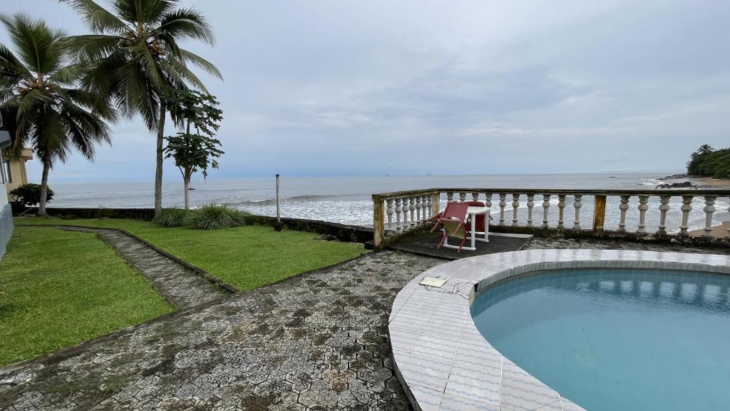 a swimming pool with a table and a chair next to the ocean at Hotel les Polygones Kribi in Kribi