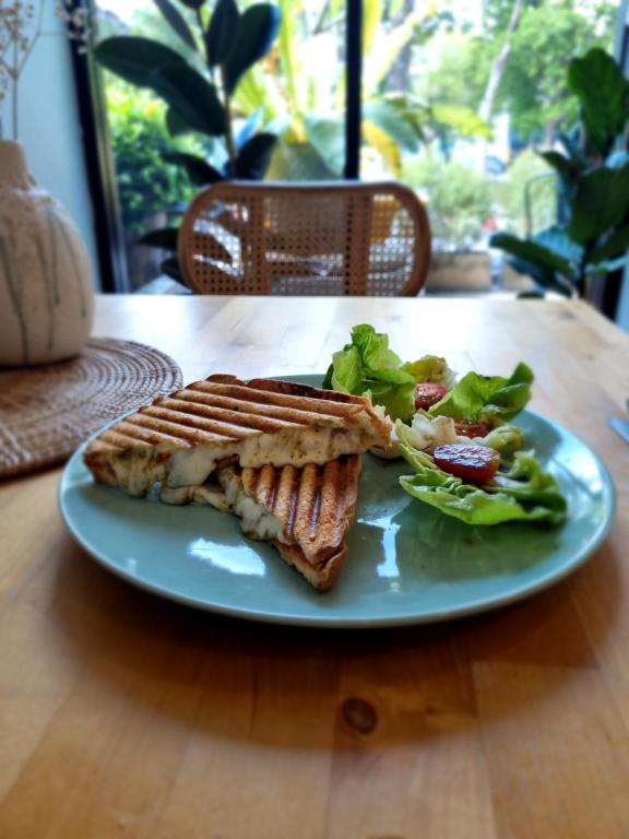 A grilled sandwich and leafy salad served beside a window.