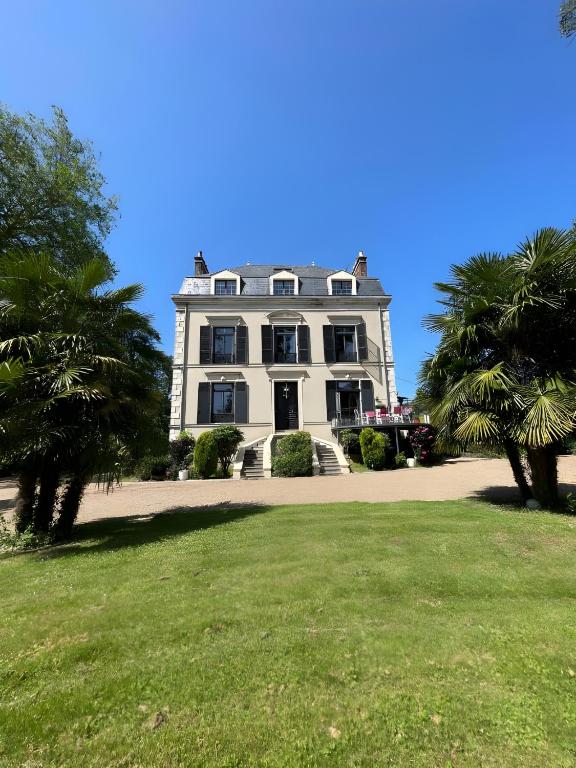 une grande maison blanche avec des palmiers devant elle dans l'établissement Domaine de la Belvaudière - 22 Pers - Piscine - Luxe -Rêve au Mans, à Saint-Pavace