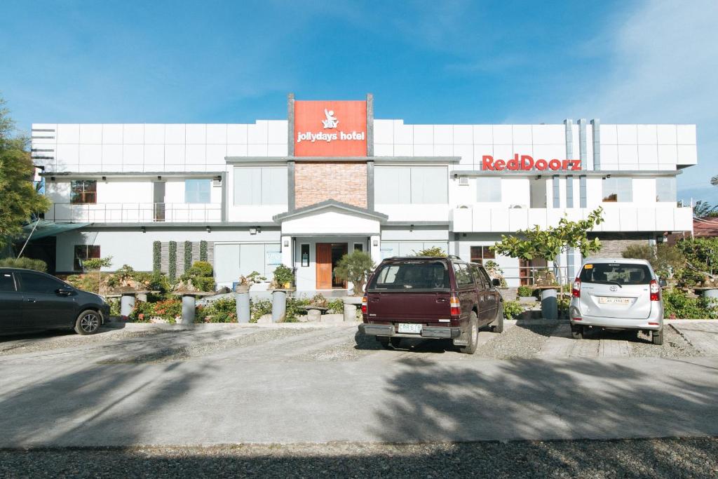 a building with two cars parked in a parking lot at RedDoorz Plus @ Jollydays Hotel Nueva Ecija in San Jose