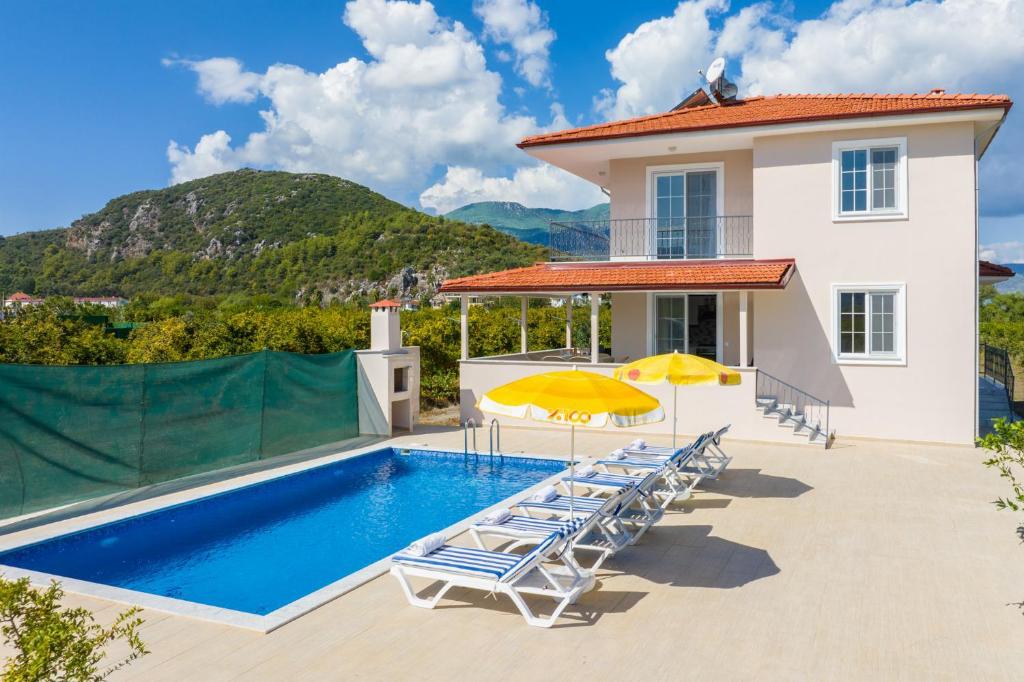 a swimming pool with chairs and umbrellas next to a house at Villa Corals in Dalyan