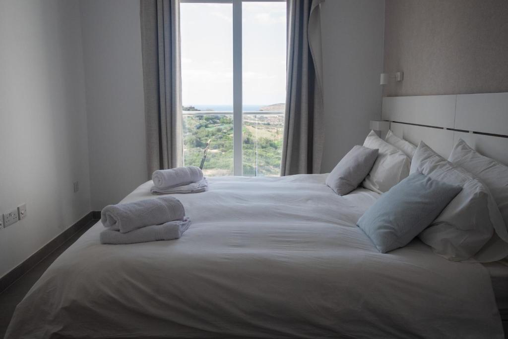 1 cama blanca grande con almohadas y ventana en Gest, en Mellieħa