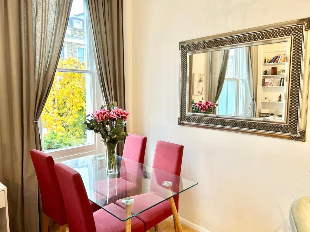 une salle à manger avec une table en verre et des chaises rouges dans l'établissement Charming 2 Beds in Chelsea By Earl's Court Station, à Londres