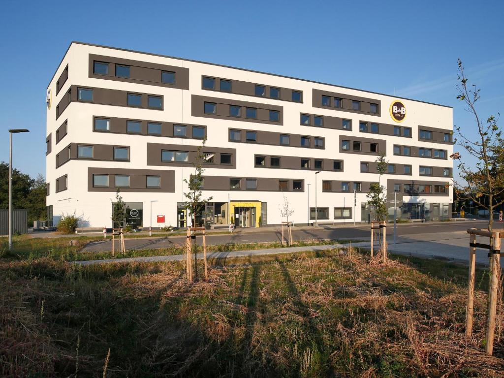 um edifício branco com árvores em frente em B&B Hotel Berlin-Airport em Schönefeld