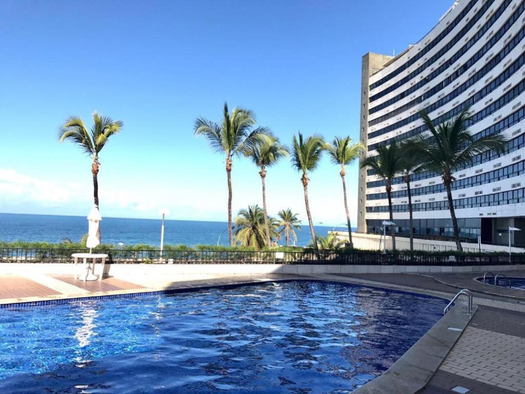 una piscina con palme di fronte a un edificio di apart hotel 2 quartos frente mar a Salvador