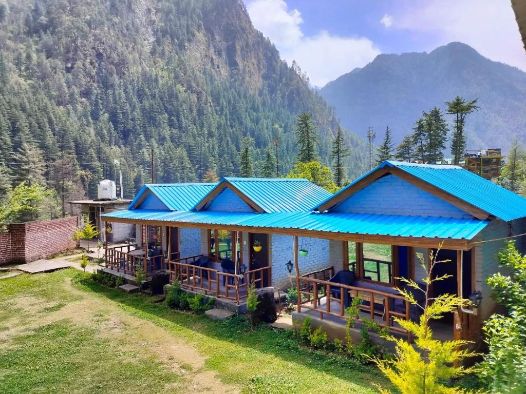 una casa con techo azul con montañas al fondo en Lee Garden Himalayan Wooden Cottages, en Kasol