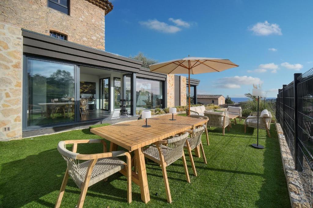 une table en bois avec des chaises et un parasol sur une pelouse dans l'établissement IMMOGROOM - Superbe villa - Piscine - Vue mer - Parking - Clim, à Vallauris
