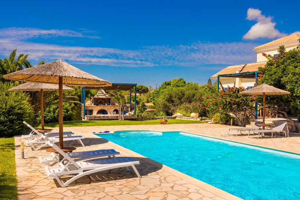 a pool with chairs and umbrellas next to a house at Villa Sapphire in Kounopetra