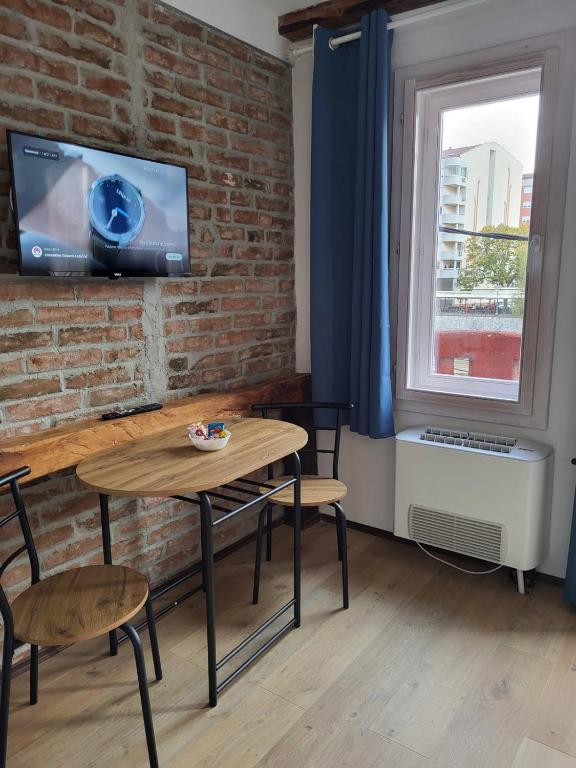 a room with a table and chairs and a tv on a brick wall at Apartment By the River in Niš