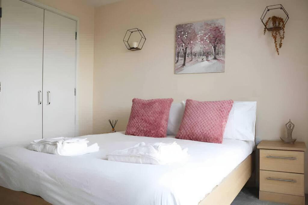 a bedroom with a white bed with pink pillows at Bright 2Bed Central Apartment in Milton Keynes