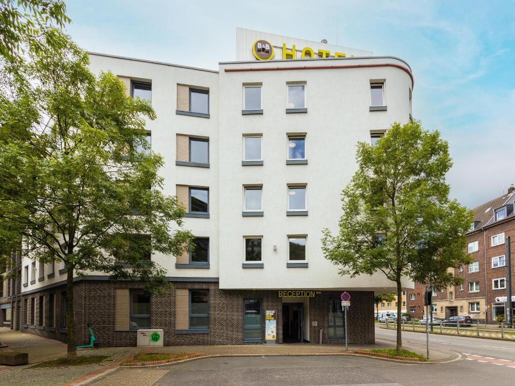 a white building with a yellow sign on top at B&B Hotel Düsseldorf City-Süd in Düsseldorf