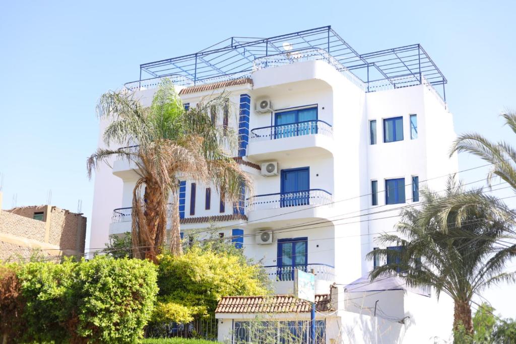 a white building with blue windows and palm trees at Villa Kaslan Apartments in Luxor