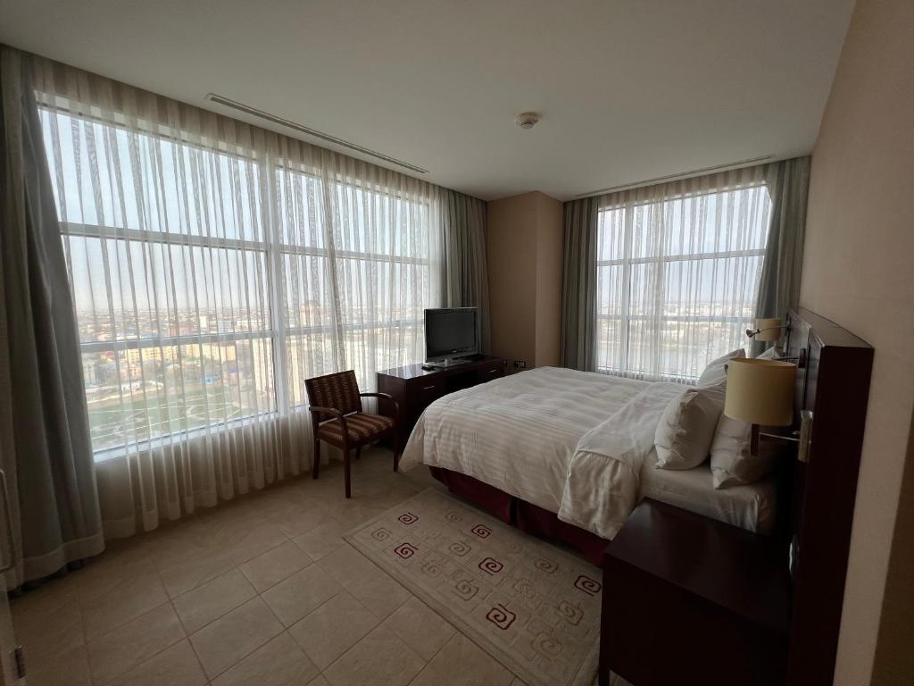 a hotel room with a bed and a desk and windows at Atyrau Executive Apartments in Atyraū