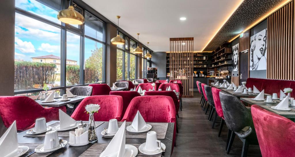 a restaurant with tables and red chairs and windows at PLAZA INN Mühldorf in Mühldorf