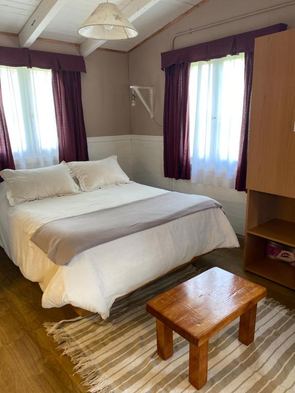 a bedroom with a bed with a table and windows at PORTAL DE LA ESTEPA in Dina Huapi