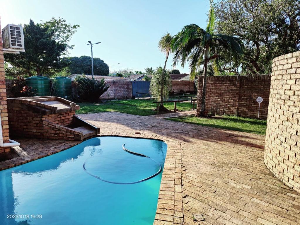 een blauw zwembad in een tuin met een bakstenen hek bij GREEN TREE in Mtubatuba