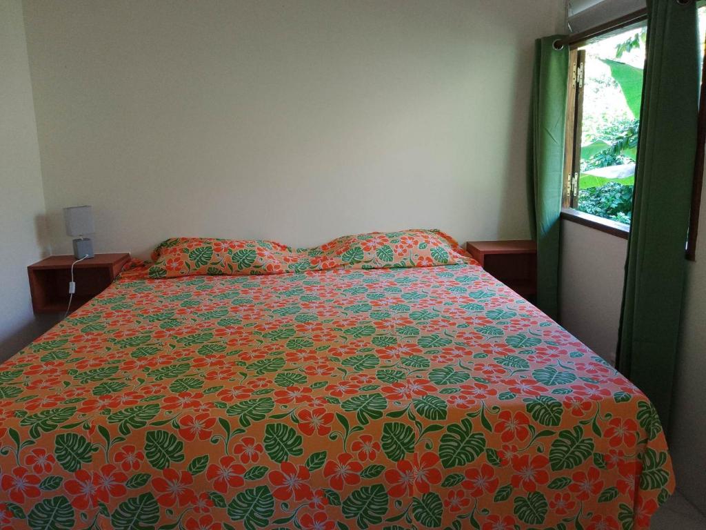 Fare Mihimana في Vaïare: غرفة نوم مع سرير مع لحاف جميل ونافذة