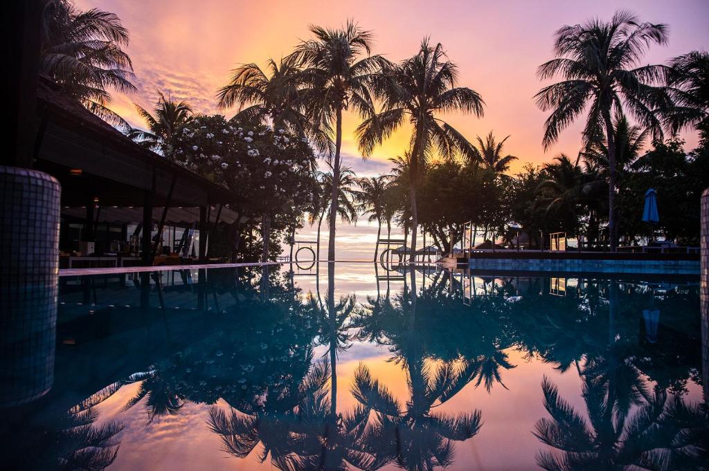 une piscine avec des palmiers et un coucher de soleil en arrière-plan dans l'établissement The Palayana Hua Hin, à Cha Am