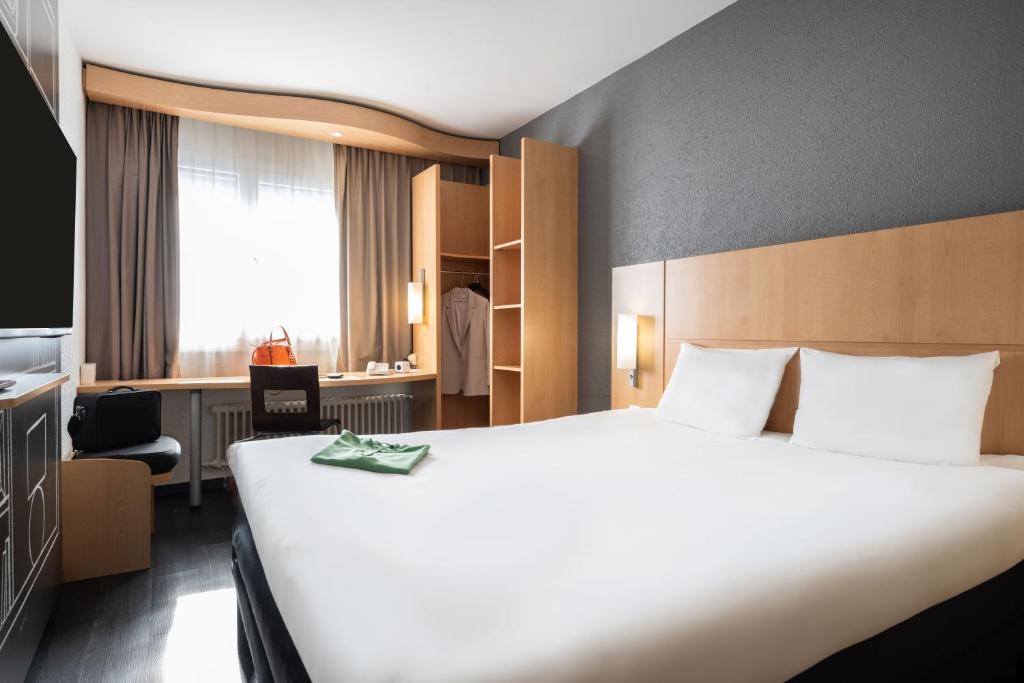 a hotel room with a large white bed and a chair at ibis Genève Centre Gare in Geneva