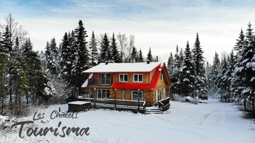 Sainte-CatherineにあるLes Chalets Tourisma - Chalet en bois rond avec spa et lac privé - Le Caribouの雪の中に赤い屋根の丸太小屋