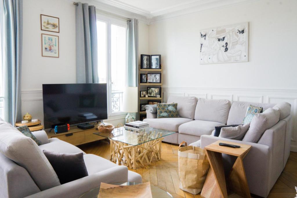 ein Wohnzimmer mit einem Sofa und einem TV in der Unterkunft EXIGEHOME-Appartement cosy avec vue sur la tour Eiffel in Saint-Cloud