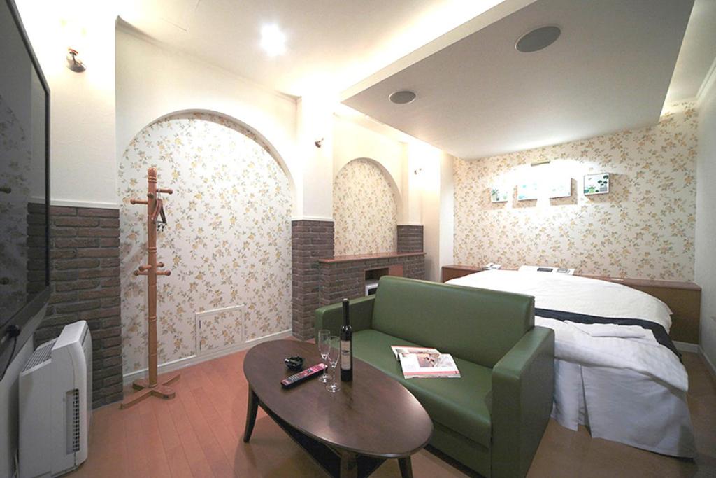 Habitación con cama, sofá verde y mesa. en Hotel LALA minato en Nagoya