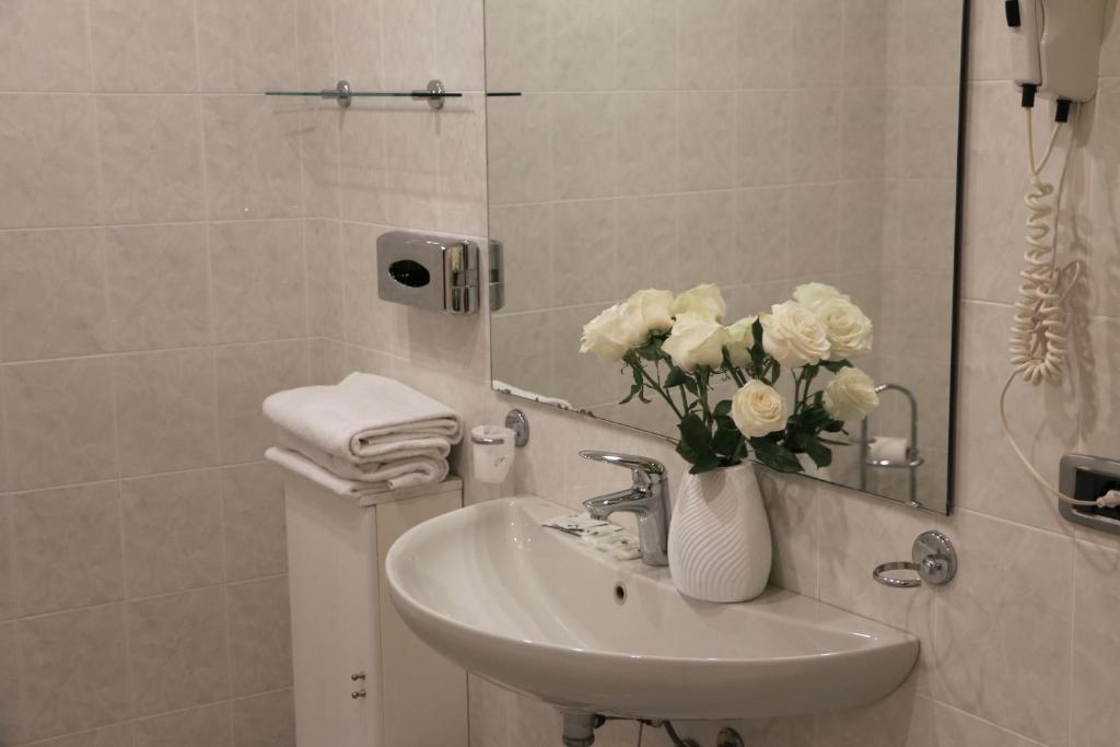 un bagno con lavandino e vaso con fiori bianchi di Hotel Kursaal BB a Salsomaggiore Terme