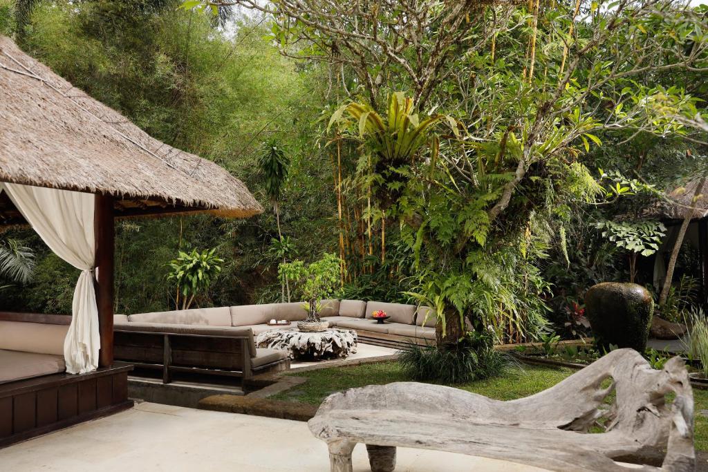 um jardim com um sofá, uma mesa e árvores em OMECURE Kaba Kaba by Nakula em Tabanan