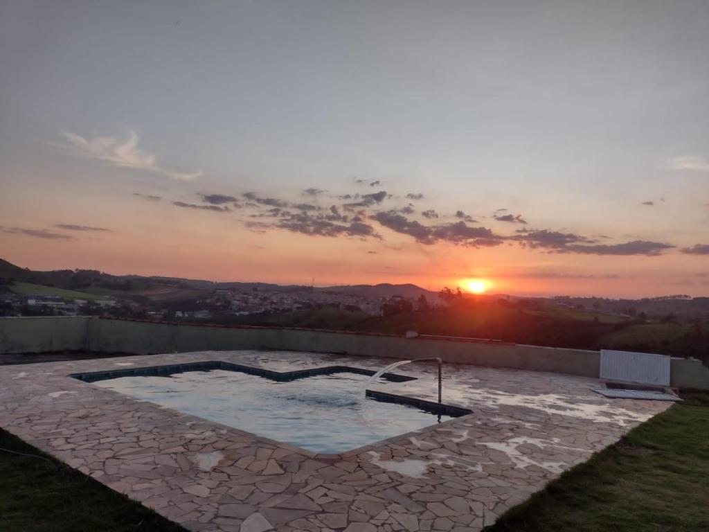 um pôr-do-sol sobre uma piscina com um pátio de pedra em Pedacinho do céu em Pinhalzinho