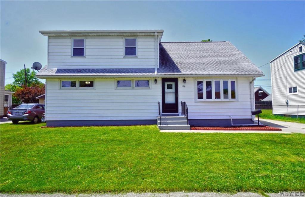 une maison blanche avec une pelouse devant elle dans l'établissement Cozy Apartments In Cheektowaga, à Cheektowaga