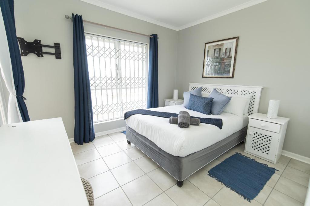 sypialnia z łóżkiem z niebieskimi poduszkami i oknem w obiekcie Shells And Bells Beachfront Apartment w mieście Summerstrand
