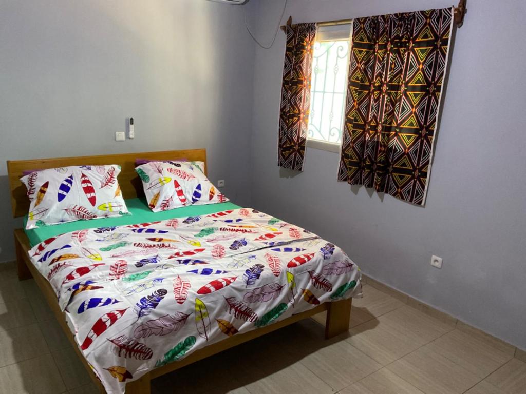 ein Schlafzimmer mit einem Bett mit einer Bettdecke und einem Fenster in der Unterkunft La Maison Du Voyageur in Kribi