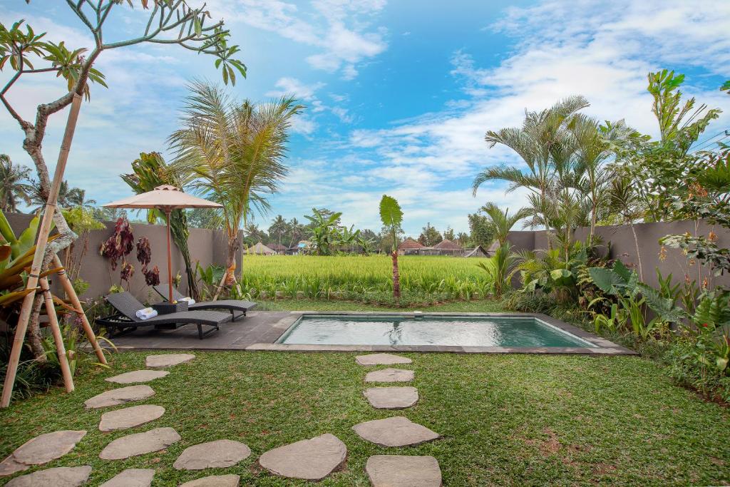 uma piscina num jardim com uma cadeira e um guarda-sol em Palasari Villa em Tegalalang