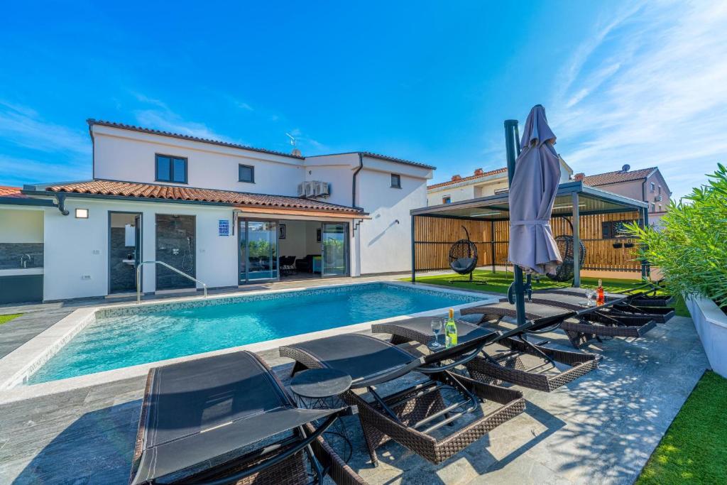a pool with chairs and an umbrella next to a house at Villa Paradise in Medulin