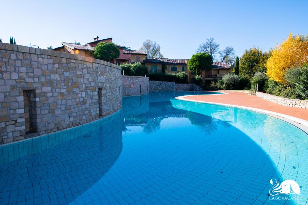 een zwembad met een bakstenen muur en blauw water bij Borgo del Torchio - App. 5H in Manerba del Garda