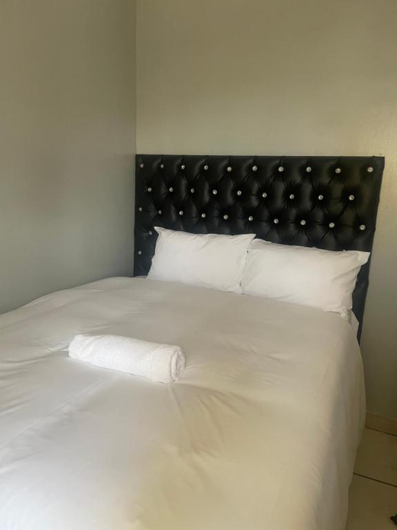 Stay Inn Lodge Boksburg في بوكسبرغ: سرير أبيض مع اللوح الأمامي الأسود والوسائد البيضاء
