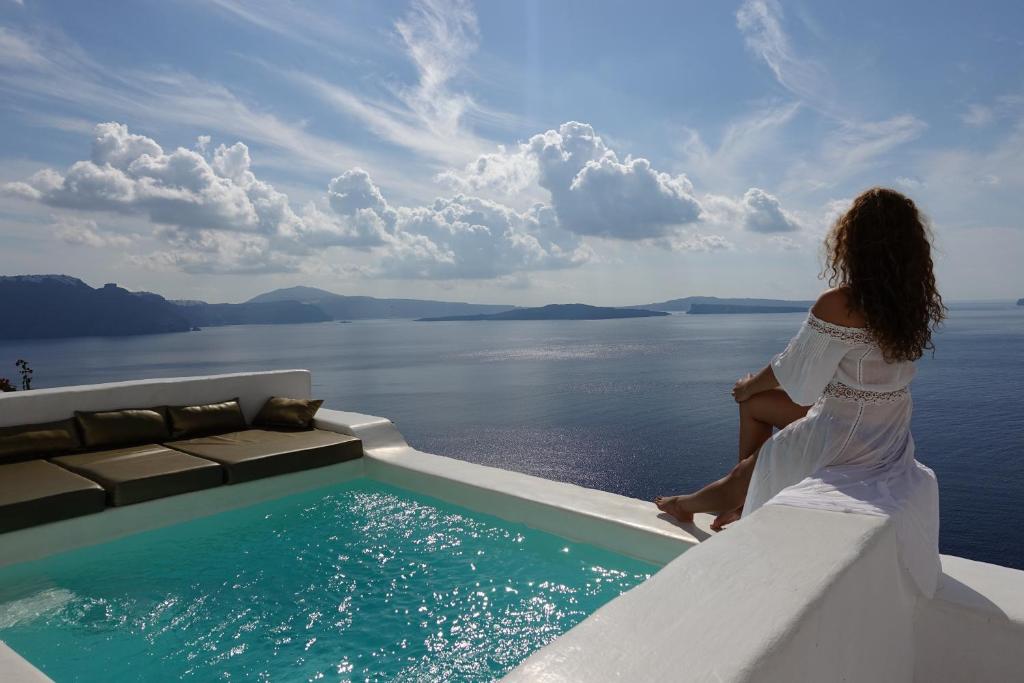a woman in a white dress sitting next to a swimming pool at Ducato Di Oia in Oia