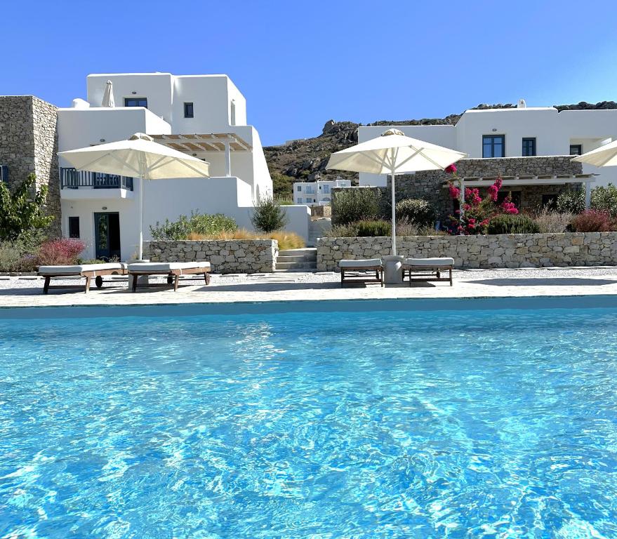 a pool with benches and umbrellas in front of a house at Archon Seaside Retreat in Plaka