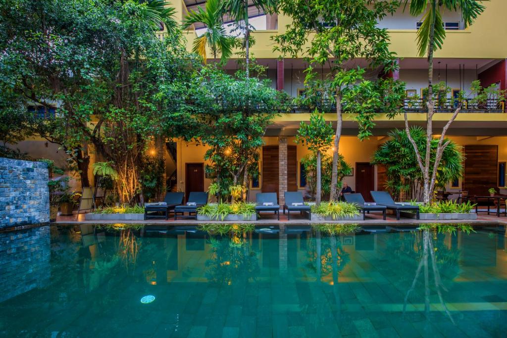 a swimming pool in front of a building with trees at Samnak Lounge in Siem Reap