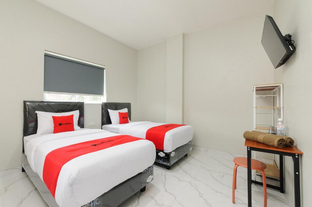 two beds in a white room with red pillows at RedDoorz near GSG UNILA Lampung in Hajimana