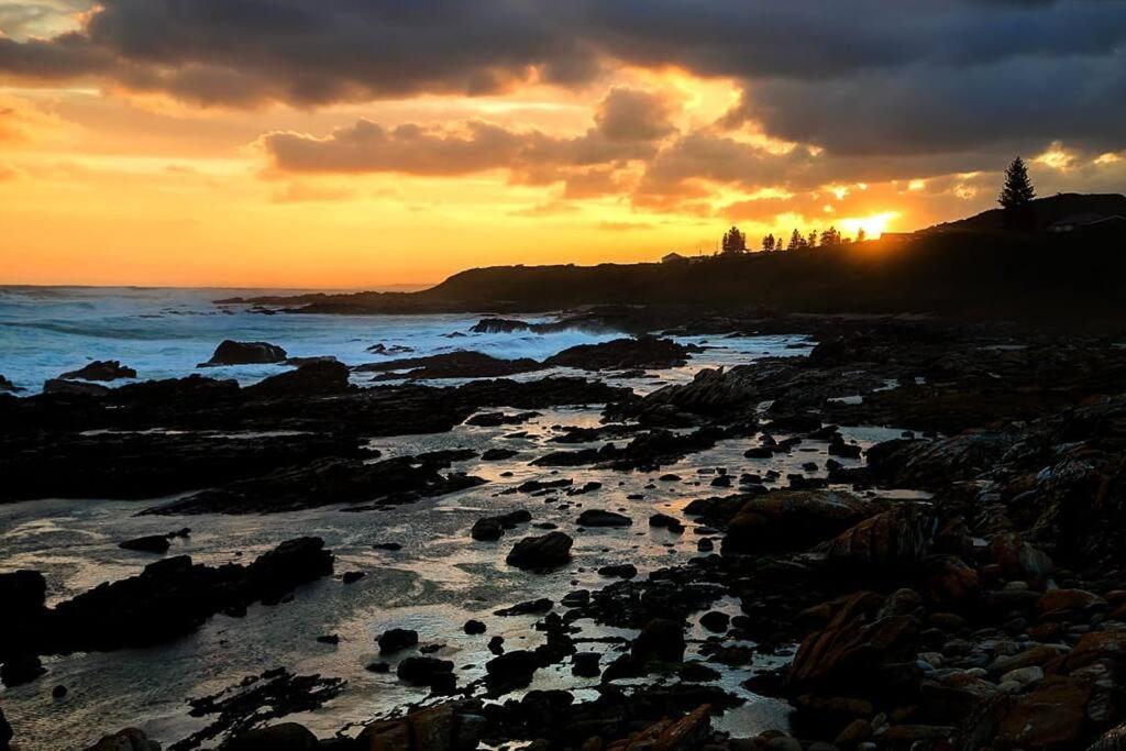 una puesta de sol sobre una playa rocosa con el océano en The Cabin on the Rock en Skoenmakerskop