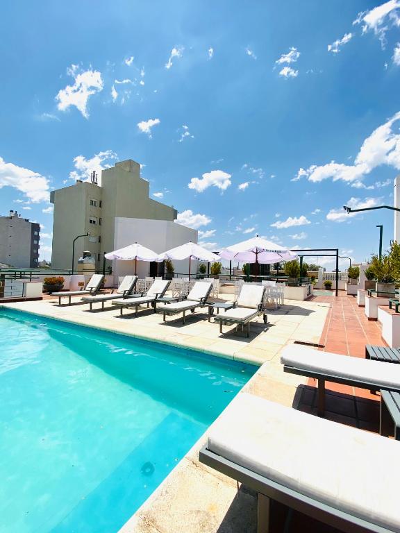 a swimming pool with lounge chairs and umbrellas on a building at HOTEL CASTELAR CORDOBA in Córdoba