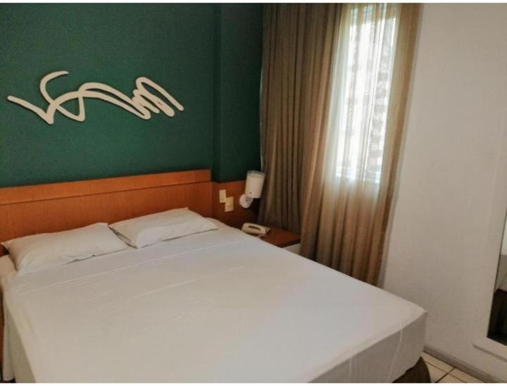 a bedroom with a white bed and a green wall at Praia do Canto Apart Hotel - Apto 102B in Vitória