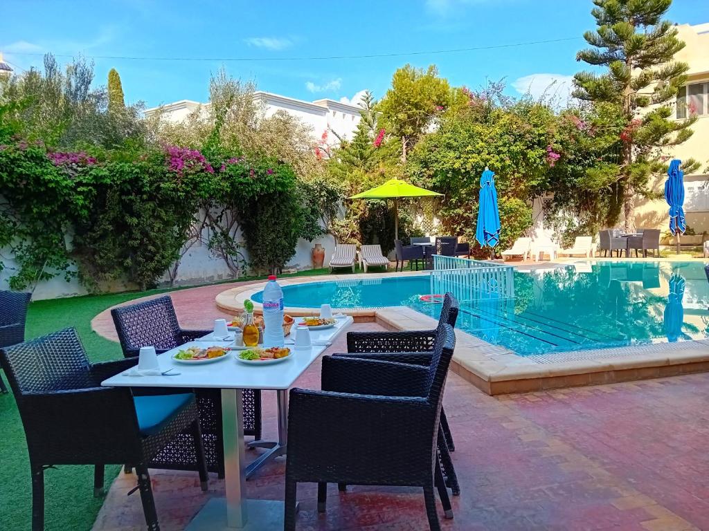 uma mesa e cadeiras ao lado de uma piscina em Hôtel Romane em Hammamet